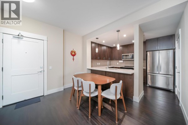 View of the dining area, kitchen, and hallway from the entrance, with a wooden dining table and chairs. - 4520 2180 Kelly Avenue, Port Coquitlam