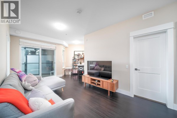 Living room space with a grey sectional sofa and a wooden media console, leading to a balcony door. - 4520 2180 Kelly Avenue, Port Coquitlam
