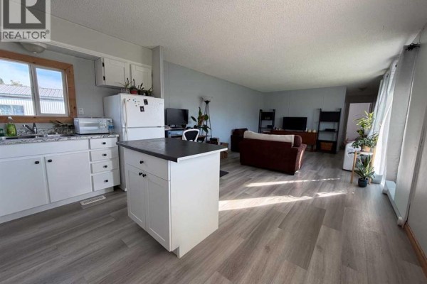Open concept kitchen and living area with white cabinets, white island, and dark brown sofas. - 4527 47 Ave Avenue N, Mayerthorpe