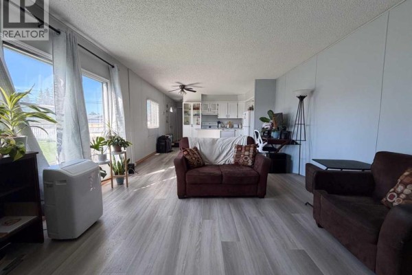 Living room with large windows, light gray walls, and dark brown seating near the kitchen area. - 4527 47 Ave Avenue N, Mayerthorpe