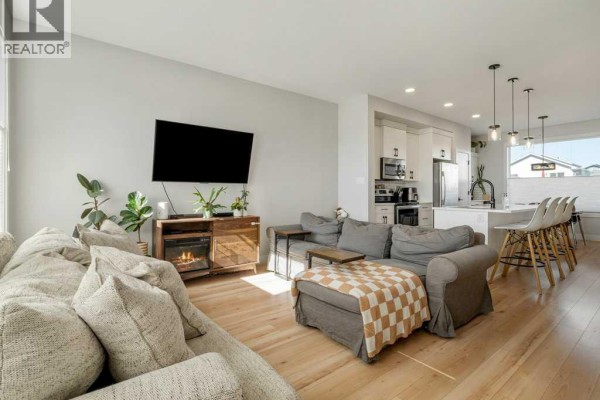 Living room and kitchen area with light wood floors, white cabinets, stainless steel appliances, and island seating. - 4531 Fairmont Gate S, Lethbridge