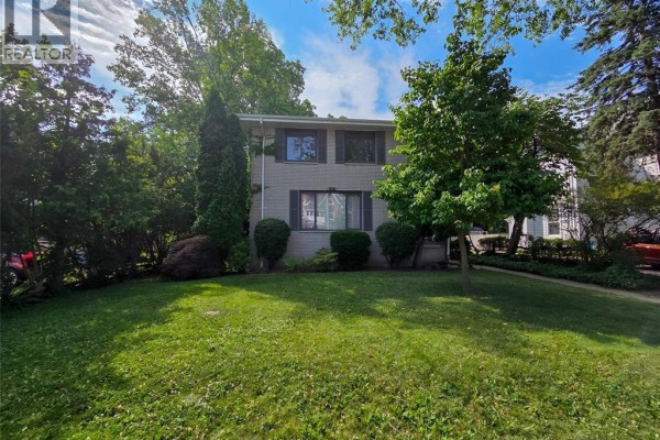 Front view of the property showing the house, driveway, and lush landscaping. - 454 King Street West, Chatham