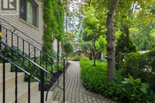 Paved walkway leading through a garden with lush green plants and trees. - 454 King Street West, Chatham