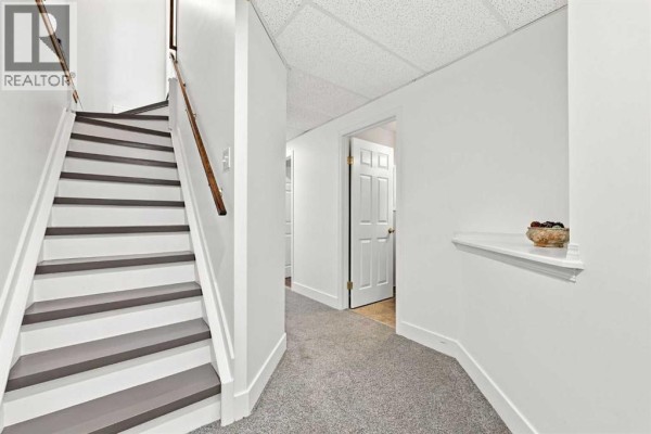 Hallway and staircase in a basement with white walls and gray carpet. - 454 Millrise Square Sw, Calgary