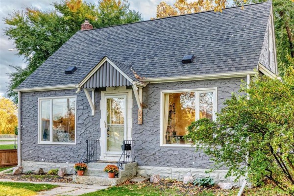 Side exterior view of the grey house, highlighting the textured siding and windows with trees nearby. - 454 Montague Avenue, Winnipeg