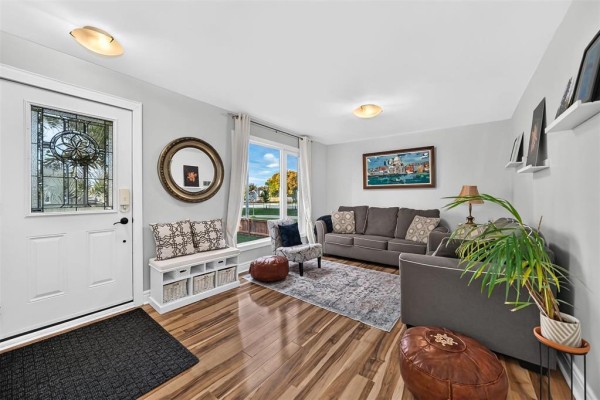 Living room with grey sofas, patterned ottoman, white bench with baskets, wood flooring, and a large window. - 454 Montague Avenue, Winnipeg