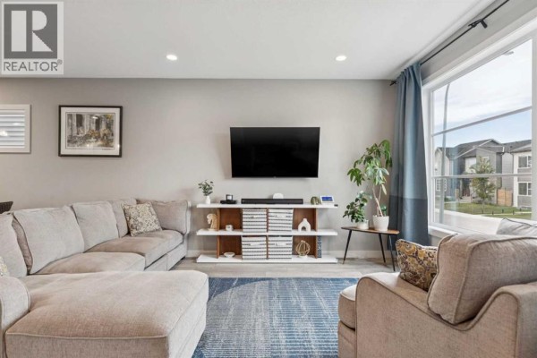 Living room with a sectional sofa, large television, entertainment unit, and a wide window. - 454 Walgrove Way Se, Calgary