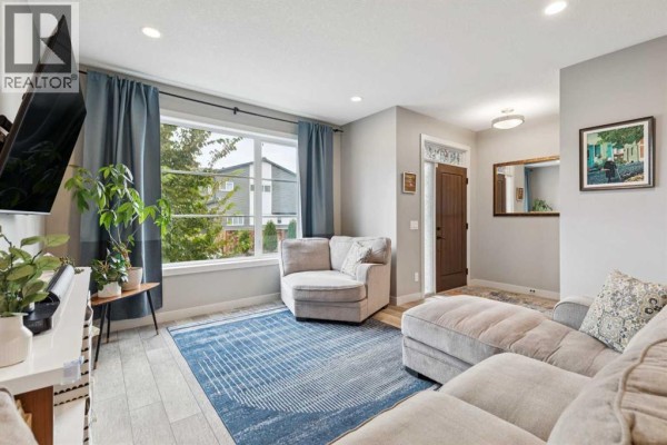 Living room with neutral-colored furniture, a blue rug, and a view through a large window to the exterior. - 454 Walgrove Way Se, Calgary