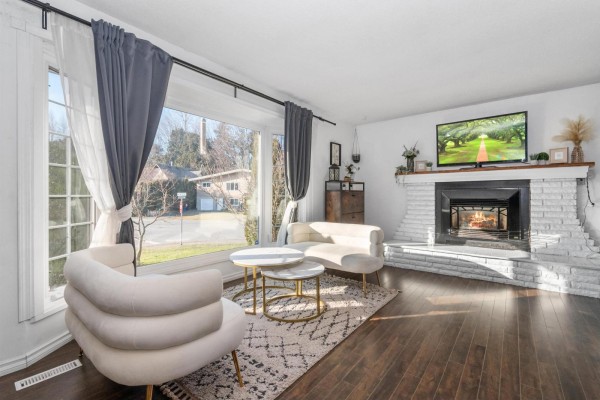 Living room with a white brick fireplace, large window, and a television on the mantle. - 45492 Spartan Crescent, Chilliwack Proper South, Chilliwack