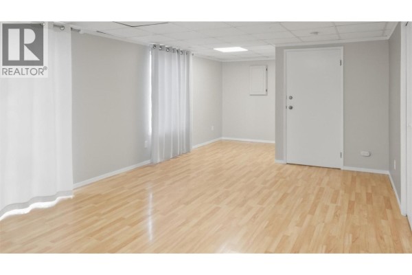 Interior view of an empty room with light wood laminate flooring and white curtains. - 455 Campbell Avenue, Kamloops