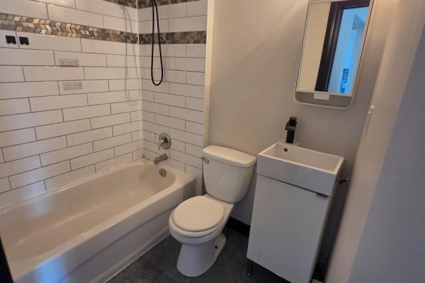 Bathroom with white tub, toilet, vanity, sink, and white tiled walls. - 455 King William Street, Hamilton