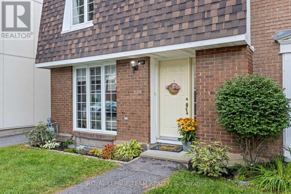 Close-up of the townhouse entrance with a yellow door, brick facade, and decorative landscaping. - 455 Kintyre Private, Ottawa