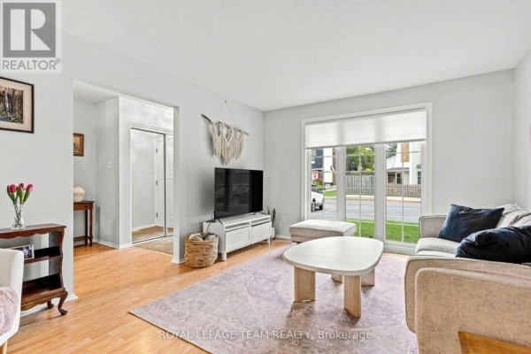Living room with light blue walls, a television on a stand, a sofa, and a large window. - 455 Kintyre Private, Ottawa