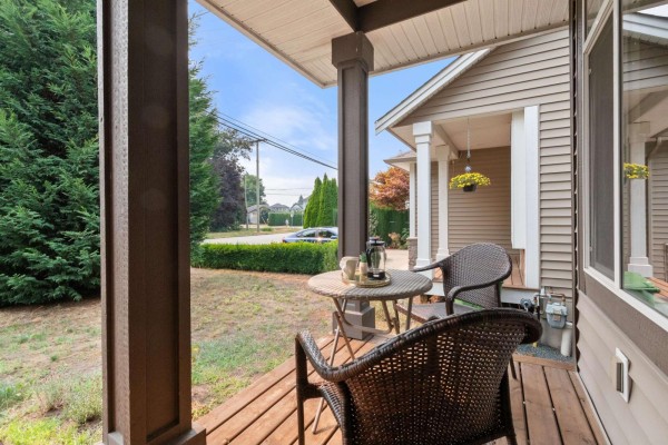 Covered front porch with wooden deck, dark wicker chairs, and small table. - 45517 Wells Road, Sardis West Vedder, Chilliwack