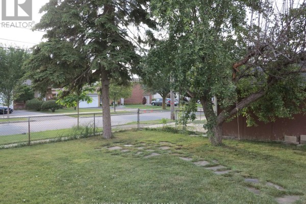 View of the street from the backyard, with a fence and trees in the foreground. - 456 Drewry Avenue, Toronto