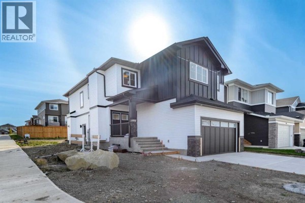 Side view of a two-story house featuring white siding, dark grey trim, and a paved driveway. - 456 Rivercrest Road, Cochrane