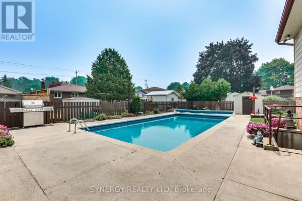 Side view of a swimming pool and patio area with a barbecue grill and wooden fence. - 456 Saulsbury Street, Strathroy Caradoc