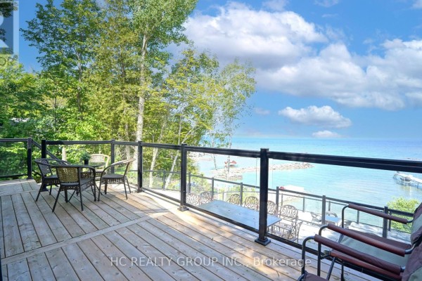 Wooden deck with glass railings, seating, and tables overlooking water and trees. - 456 Silver Birch Drive, Tiny