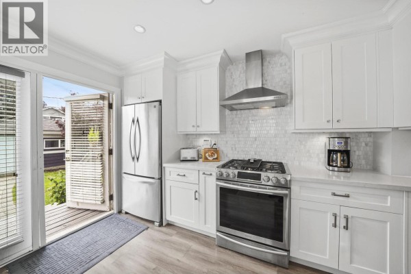 Open concept kitchen and living space with white cabinets, a breakfast bar with stools, and a home office area. - 4560 Pender Street, Burnaby