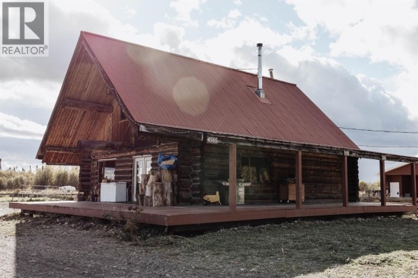 Log cabin exterior showcasing its wooden structure, red roof, and a covered porch area. - 4565 Holmes Road, Prince George