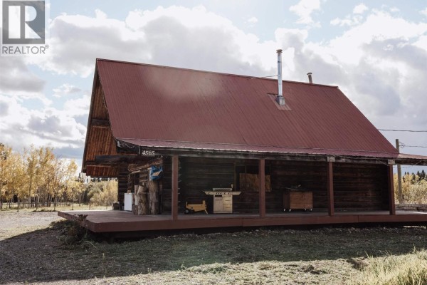 Side view of a rustic log cabin with a red metal roof and a wide wooden deck. - 4565 Holmes Road, Prince George