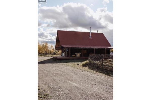 Gravel driveway leading to the side of a wooden log cabin with a red roof. - 4565 Holmes Road, Prince George