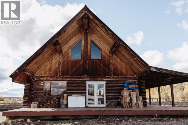 Front facade of a log cabin featuring a prominent A-frame roof, double doors, and a large deck. - 4565 Holmes Road, Prince George