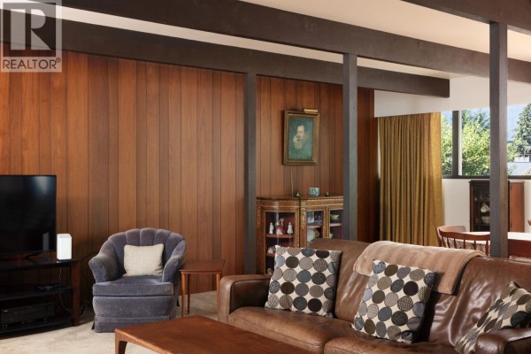Living room with brown leather sofa, armchair, wood-paneled walls, and built-in cabinet. - 4568 Marineview Crescent, North Vancouver