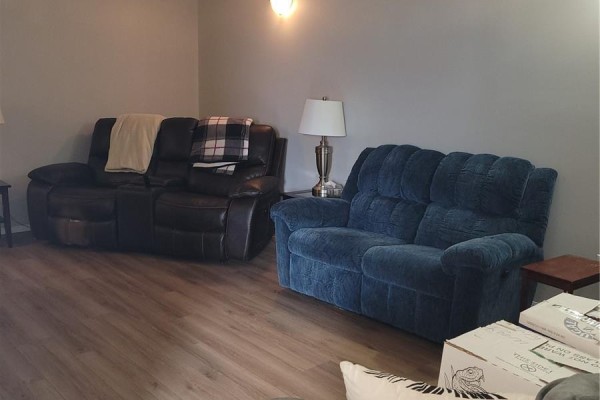 Living room with a brown leather recliner and a blue fabric loveseat on a wood-look floor. - 457 Brooklyn Crescent, Warman