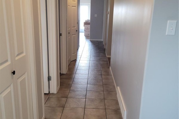 Hallway with tiled floor and white doors leading to rooms. View towards a brightly lit door. - 457 Brooklyn Crescent, Warman