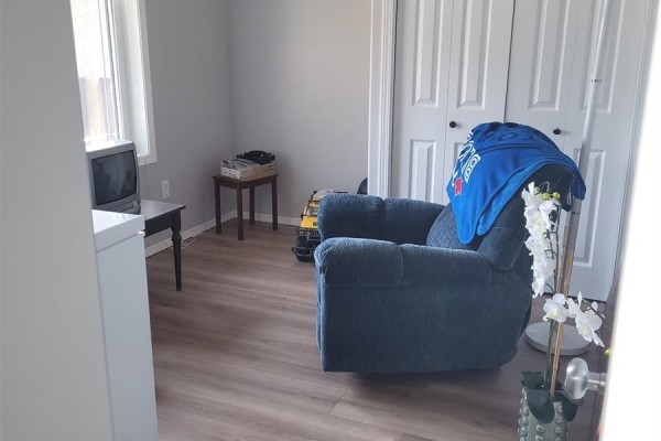 Room with blue recliner, small television, and large double doors. Wood-look flooring. - 457 Brooklyn Crescent, Warman