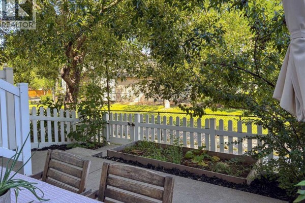 Backyard patio with wooden chairs, garden beds, and white picket fence. - 457 Elgin Gardens Se, Calgary