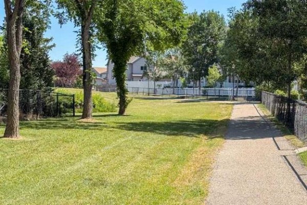 Grassy park with a walking path and trees, bordering a fenced area. - 457 Elgin Gardens Se, Calgary