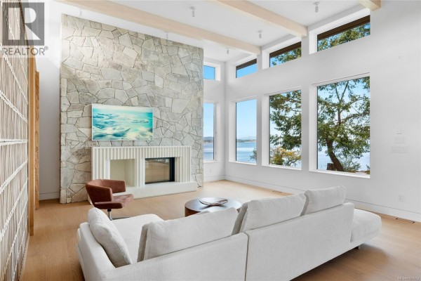 Bright living room with stone fireplace, large windows, and views of the water - 4570 Bissenden Pl, Saanich