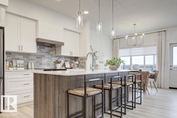 Open-concept kitchen with white cabinets, a large island with seating, and stainless steel appliances. - 4570 Chegwin Wd Sw, Edmonton