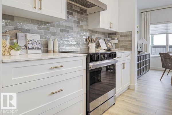 Close-up of white kitchen cabinets, subway tile backsplash, and stainless steel oven. - 4570 Chegwin Wd Sw, Edmonton
