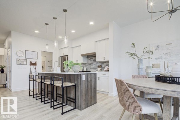 Kitchen and dining area with light wood flooring, a large island, and a dining table with chairs. - 4570 Chegwin Wd Sw, Edmonton