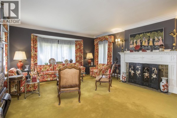 Living room seating area with two antique chairs, a patterned sofa, a glass coffee table, and a fireplace. - 4576 Connaught Drive, Vancouver