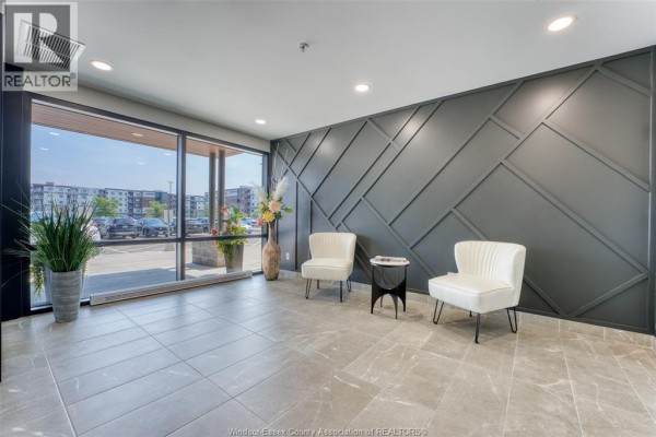 Lobby seating area with two white chairs, a small table, and a large window. - 4578 Huron Church Line Road Unit# 502, Lasalle