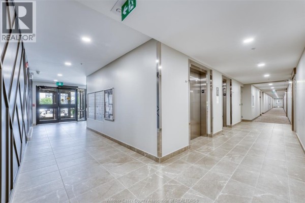 Long apartment building hallway with tiled floor, elevators, and lit ceiling panels. - 4578 Huron Church Line Road Unit# 502, Lasalle