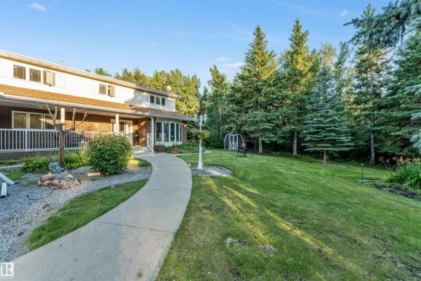 Covered porch of a brick house with wicker furniture and sliding glass doors to the entrance. - #458 23109 Twp Road 514, Rural Strathcona County