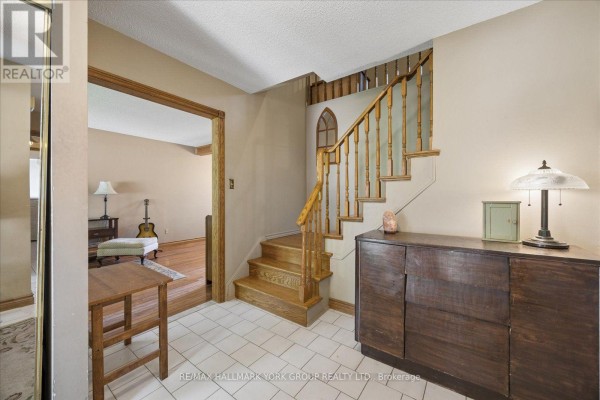 Interior foyer with white tile flooring, stairs to the upper level, and a dark wood credenza. - 458 Chester Avenue, Newmarket