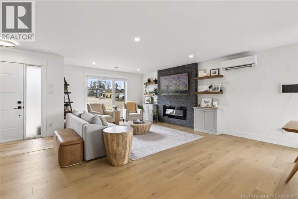 Living room with light wood floors, gray sofa, accent chairs, and a stone fireplace feature. - 458 Gaspé Street, Dieppe