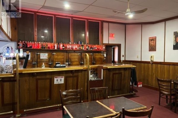 Wooden bar area with bottles on shelves and tables in the foreground. - 458 Queen St, Sault Ste  Marie