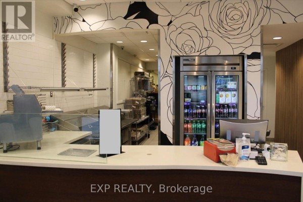 Service counter with glass sneeze guards, stainless steel kitchen equipment, and a refrigerator. - 458 Rideau Street, Ottawa