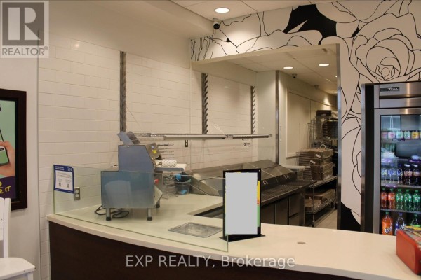 Close-up of a commercial kitchen counter with glass barriers, stainless steel equipment, and beverage cooler. - 458 Rideau Street, Ottawa