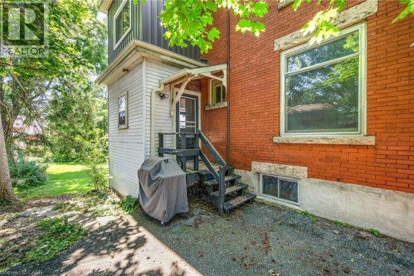 Side and back exterior of the house with a grill, wooden stairs, and windows. - 458 Woolwich Street, Guelph