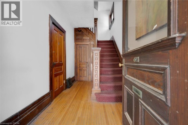 Interior hallway with hardwood floors, a wooden staircase with red carpet, and dark wood trim. - 458 Woolwich Street, Guelph