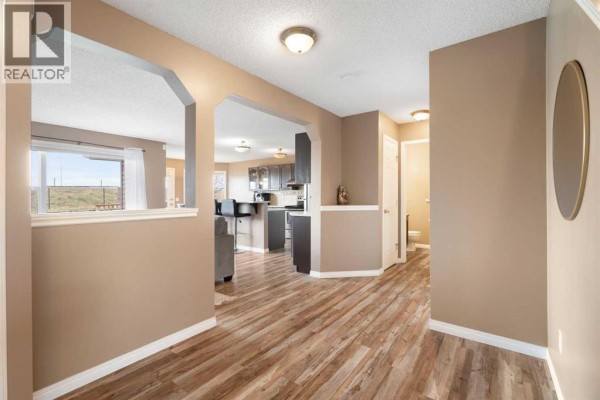 Interior hallway with tan walls, wood-look flooring, and archways leading to living and kitchen areas. - 459 Citadel Meadow Bay Nw, Calgary
