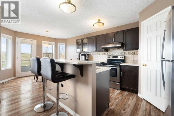 Kitchen island with two dark leather stools, white countertop, and stainless steel appliances in a tan room. - 459 Citadel Meadow Bay Nw, Calgary